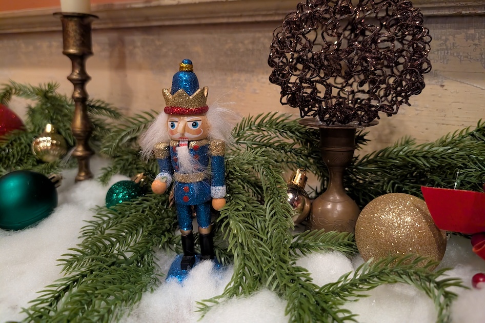 Nutcracker sitting on a mantle decorated with Christmas decorations